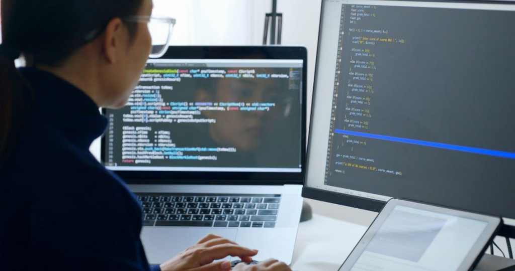 female IT employee writing code with two screens