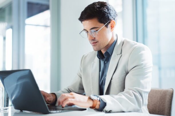 IT professional in glasses working on a laptop in a modern bright office