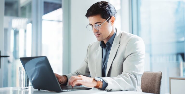 IT professional in glasses working on a laptop in a modern bright office