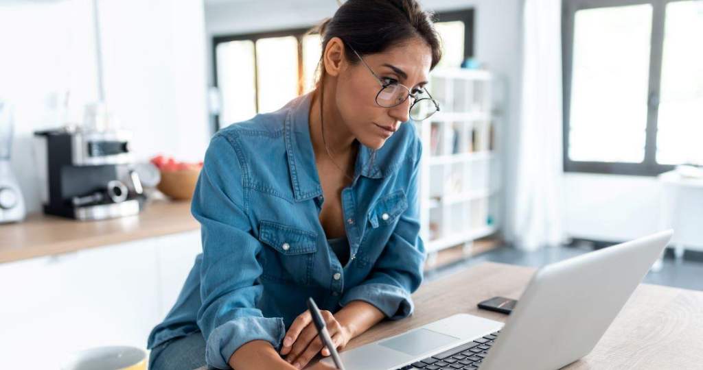 young woman doing research on a laptop and taking hand-written notes