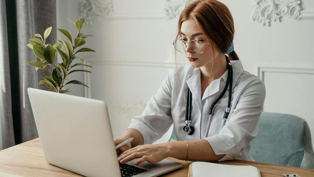 female doctor sitting at a desk and typing on a laptop