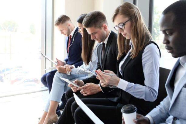 five job applicants sitting in a row filling out a form and waiting to interview