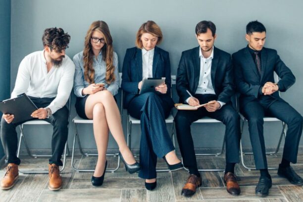 three male and two female candidates sitting on individual chairs in a row waiting to interview