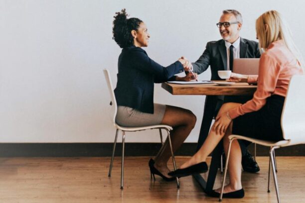 three people in business attire sitting at a table and shaking hands