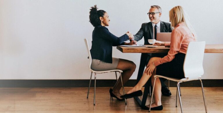 three people in business attire sitting at a table and shaking hands