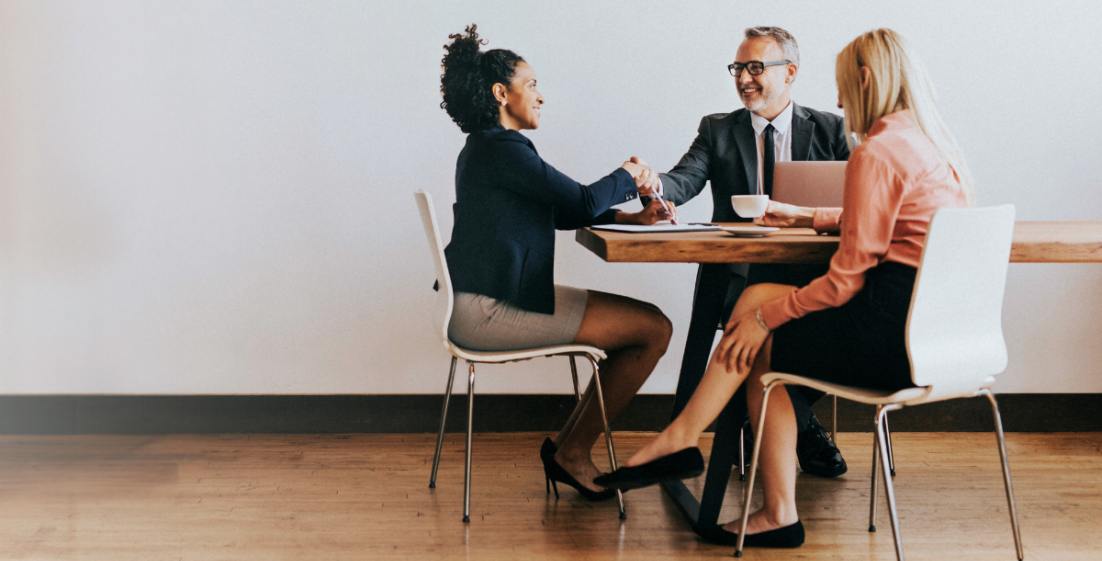 three people in business attire sitting at a table and shaking hands