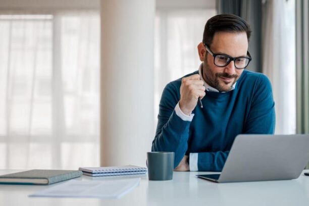 man in glasses working at a desk on a laptop
