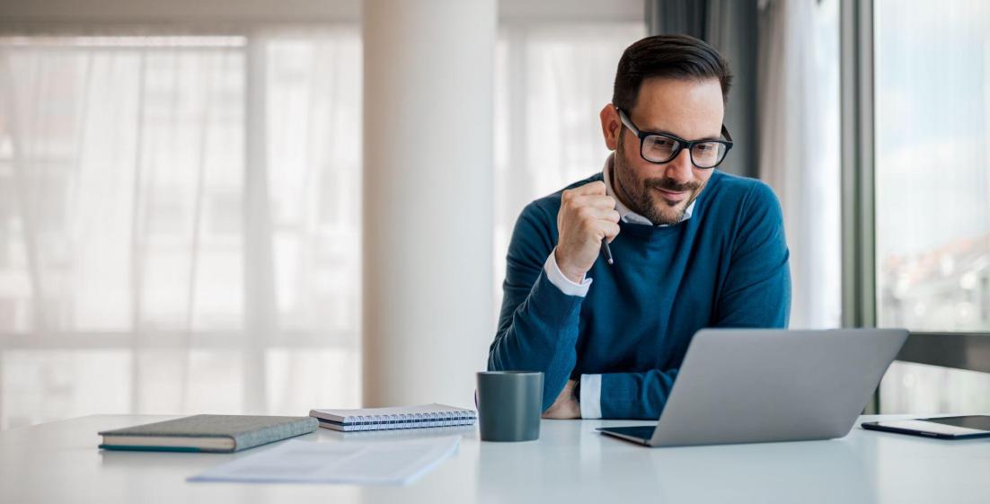 man in glasses working at a desk on a laptop