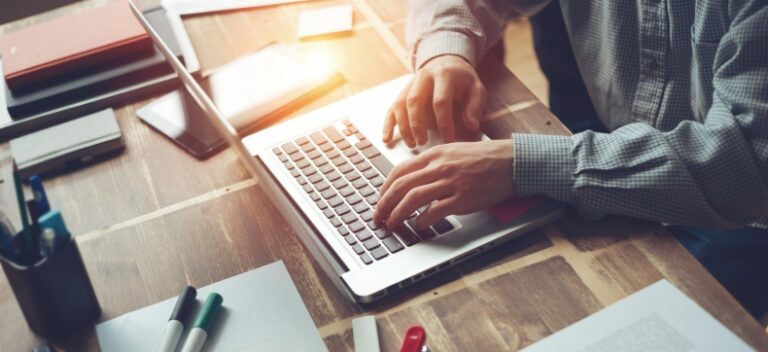 Man typing on a laptop at a cluttered wooden desk