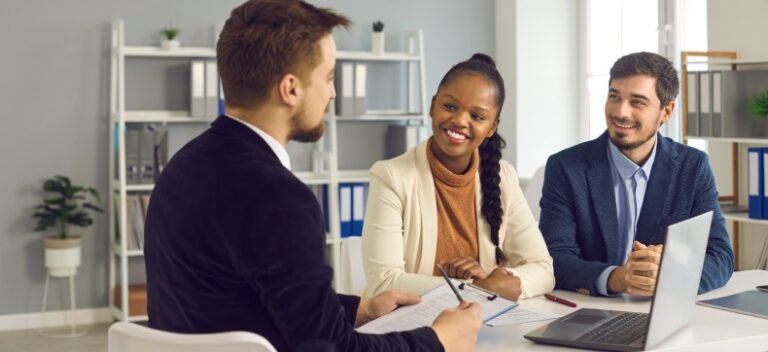 Diverse professionals in smiling discussion at office table with laptop and notes