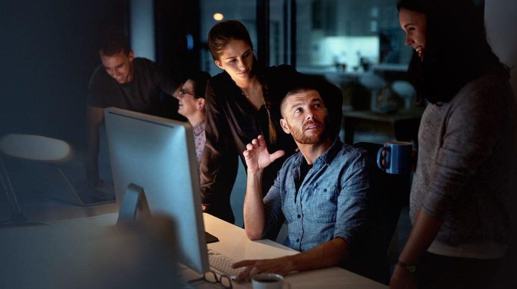 Team collaborating around computer in modern office at night