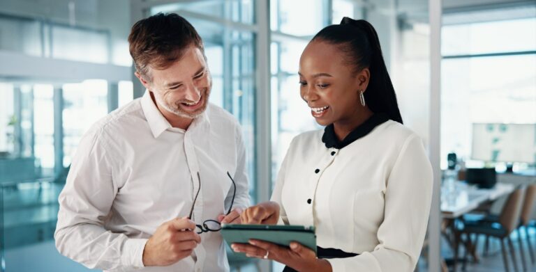 Two business leaders smiling while reviewing a tablet in a modern office