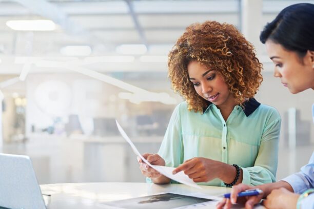 Two HR professionals reviewing hiring documents together in a bright office