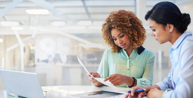 Two HR professionals reviewing hiring documents together in a bright office
