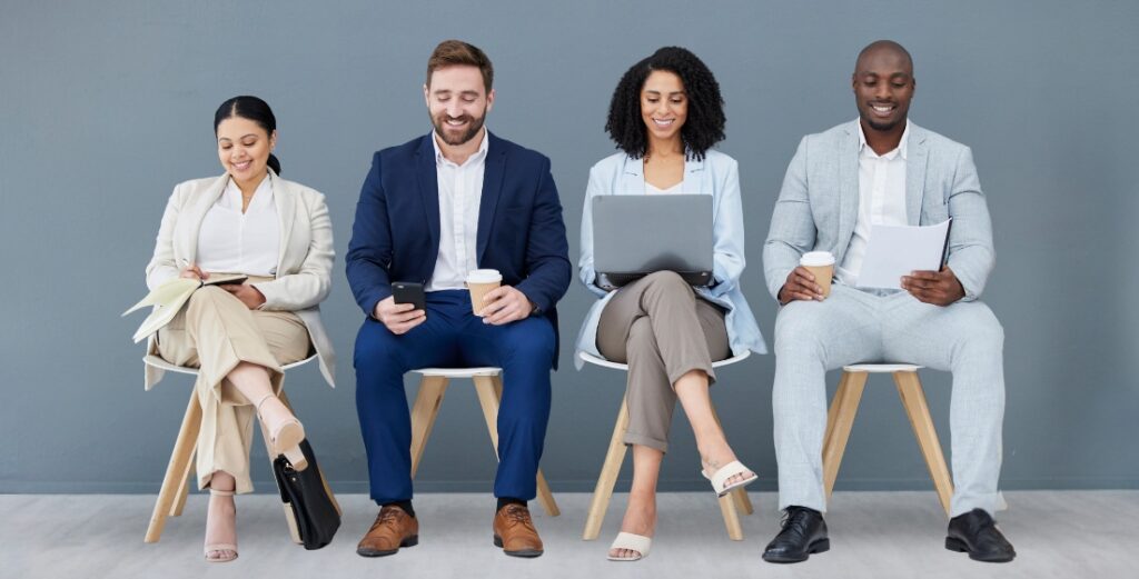 Four diverse job candidates waiting with laptops, phones, and resumes.