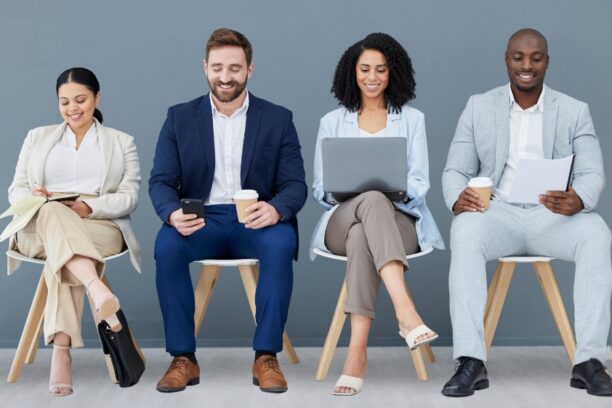 Four diverse job candidates waiting with laptops, phones, and resumes.